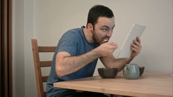 朝食を食べながらタブレットでニュースを読んでいる若い男の人 — ストック動画