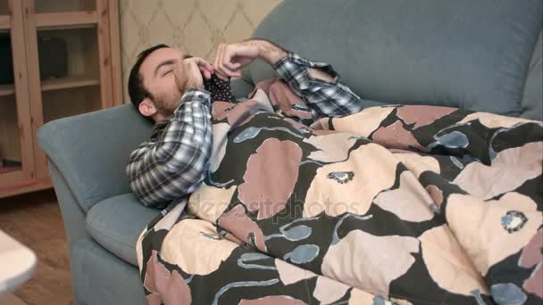 Mladý muž předstírá, že být nemocný s chřipkou ležet na pohovce — Stock video