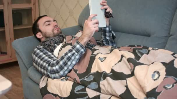 Nemocný mladík pomocí tabletového počítače ležel na pohovce — Stock video