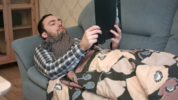 Young man reading book while lying sick on the sofa — Stock Video