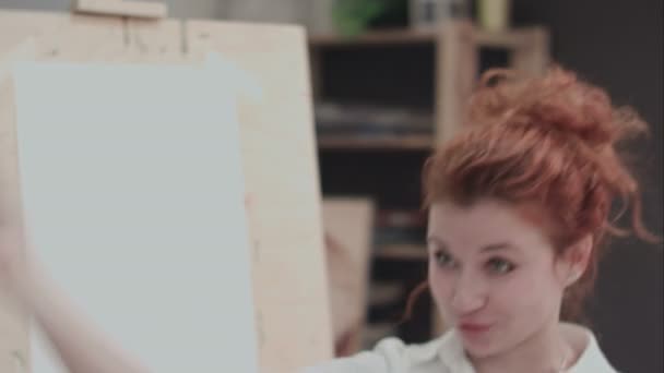 Молода жінка-художник біля мольберта описує творчий процес — стокове відео