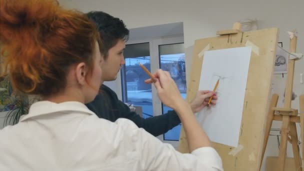 Vrouwelijke artiest onderwijs jonge man om te tekenen met potlood — Stockvideo