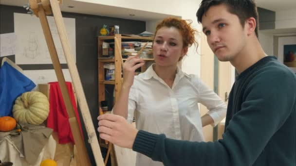 Künstlerin hilft ihrem männlichen Schüler, auf Staffelei zu zeichnen — Stockvideo