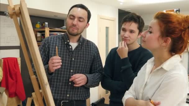 Усміхнені студенти та вчителька жіночого мистецтва аналізують твори мистецтва на мольберті — стокове відео