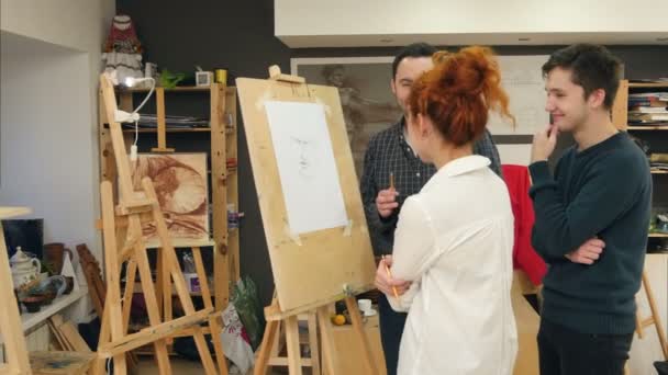 Tres alegres estudiantes de arte discutiendo pintura en estudio — Vídeos de Stock