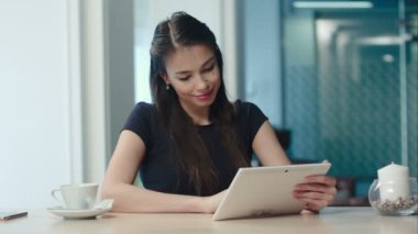 Bir kahve dükkanında tablet bilgisayar kullanan mutlu genç kadın