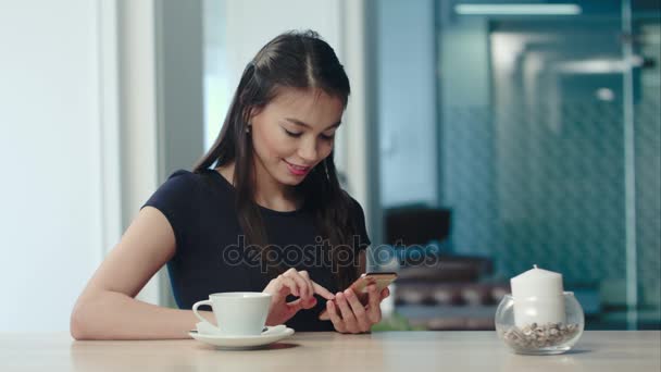 Sorrindo mulher bonita mensagens de texto no smartphone em um café — Vídeo de Stock