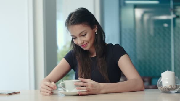 Drömmande ung kvinna håller en kopp kaffe och sång på café — Stockvideo