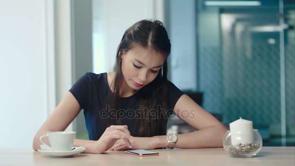 Atractiva joven mujer disfrutando del café mientras revisa su teléfono en un café — Vídeos de Stock