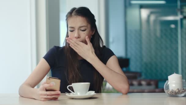 Junge gelangweilte Brünette gähnt und dehnt sich und trinkt Kaffee in einem Café — Stockvideo