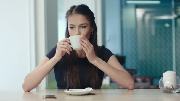 Mooie jonge vrouw zitten in een café met een kopje koffie — Stockvideo