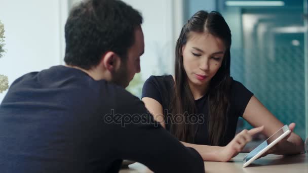 Jeune couple assis à table en utilisant une tablette numérique à la cafétéria — Video