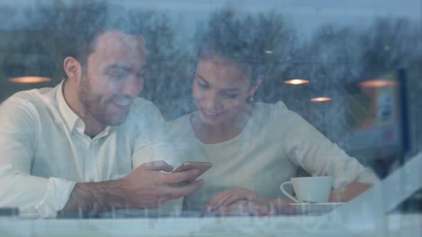 Счастливая молодая пара сидит за столом, используя телефон в кафетерии — стоковое видео