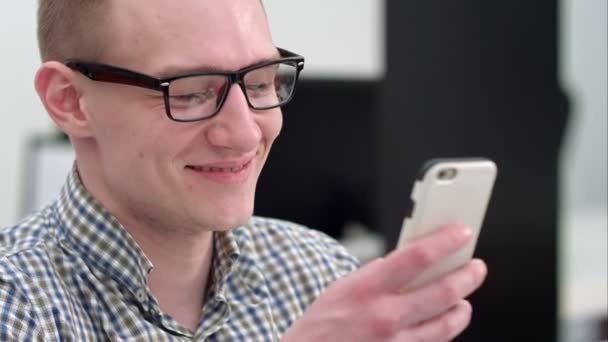 事務所スマート フォンでテキスト メッセージで笑いの若い男 — ストック動画