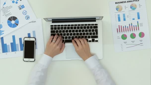 Женщины руки печатают на ноутбуке в офисе стол с графиком статистики — стоковое видео