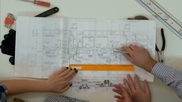 Молодые архитекторы проверяют размеры чертежей с помощью делителя и линейки — стоковое видео