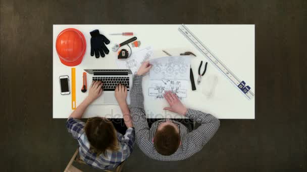 Architect bezig met blauwdrukken terwijl vrouwelijke collega typen op laptop — Stockvideo