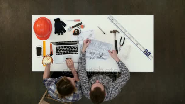 Vrouwelijke architect over tekening met haar collega terwijl het eten van de lunch en typen — Stockvideo