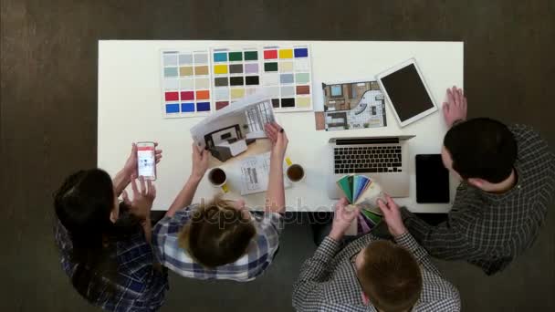 Four designers discussing layouts and color samples at office desk — Stock Video