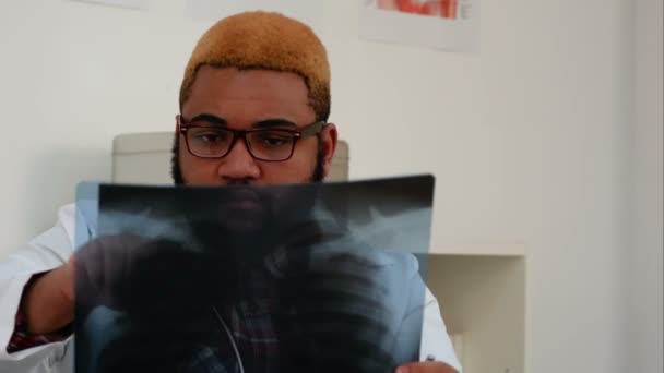 Afroamerican arts xray analyseren en knikken zijn hoofd in medische kantoor — Stockvideo