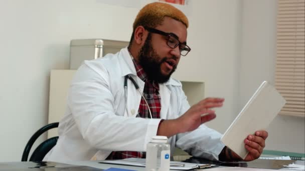 Africano americano médico do sexo masculino explicando os resultados xray para o paciente através de chamada de vídeo em tablet — Vídeo de Stock