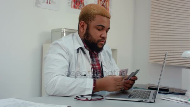 Młody lekarz, liczenie pieniędzy na jego biurko — Wideo stockowe