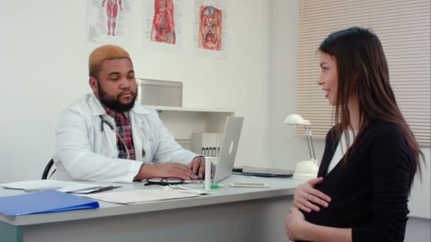 Mujer embarazada visitando joven sonriente médico masculino — Vídeo de stock