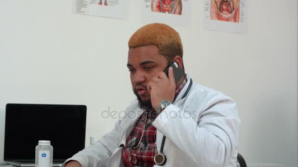 Médico afroamericano hablando por teléfono haciendo esperar a su paciente — Vídeos de Stock