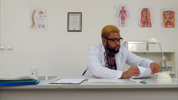 Афроамериканский врач, работающий с медицинскими формами и документами в офисе — стоковое видео
