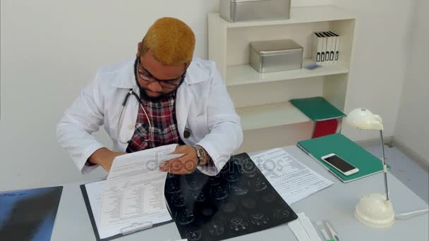Médecin afro-américain remplissant des formulaires médicaux et répondant à des appels téléphoniques à son bureau 