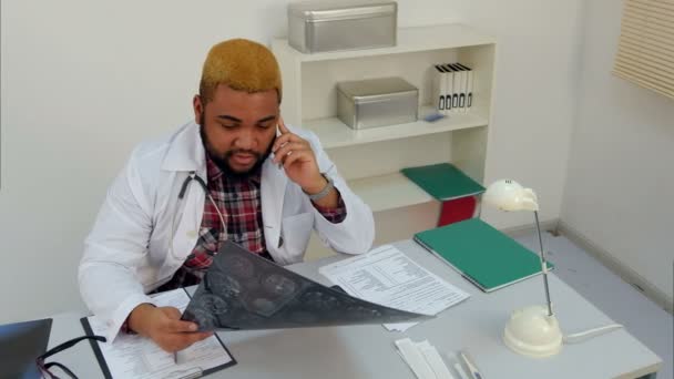 Médico afroamericano que tiene una llamada telefónica sobre los resultados de rayos X — Vídeos de Stock