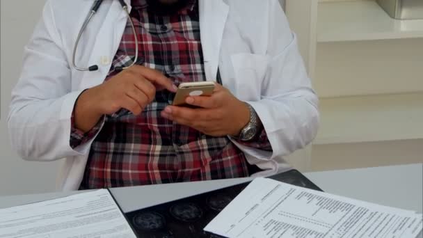 Αρσενικό ο γιατρός γραπτών μηνυμάτων σε ένα smartphone που κάθεται στο γραφείο του — Αρχείο Βίντεο