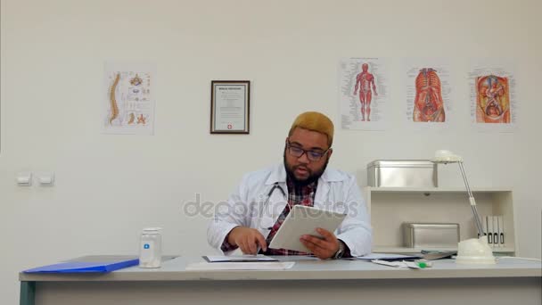 Médecin afro-américain travaillant avec une tablette numérique dans son bureau — Video