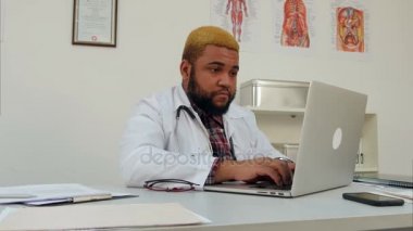 Konsantre Afroamerican genç doktor masasında dizüstü bilgisayar kullanarak