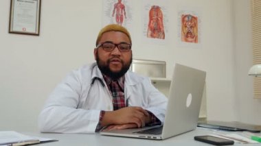Afrika kökenli Amerikalı doktor ofisinde oturan kameraya konuşurken