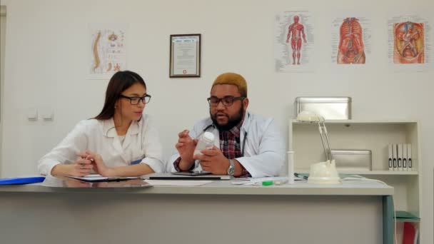 Afroamerican erkek doktor hap kadın stajyer notlar sırasında kavanoz holding — Stok video