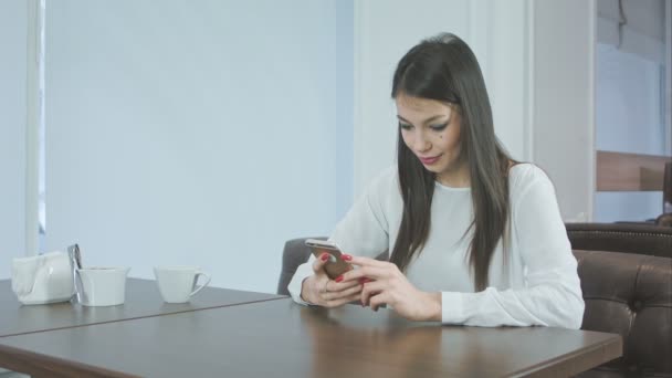 Ung kvinna i café meddelanden på telefonen och leende — Stockvideo