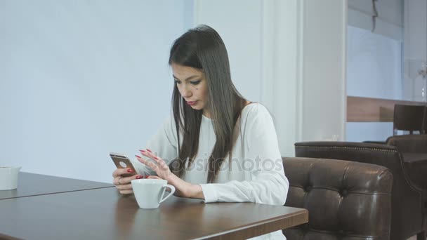 Mooi meisje in een café met behulp van telefoon en rondkijken — Stockvideo