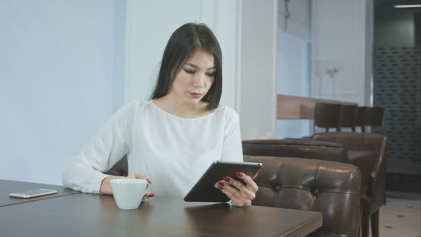 Ung kvinna med digital surfplatta medan du dricker kaffe eller te på ett kafé — Stockvideo