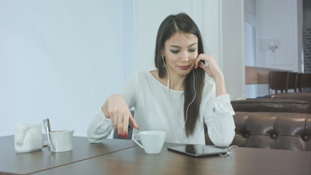 Ásító unatkozni lány segítségével tabletta, és kávét iszik egy kávézóban — Stock videók