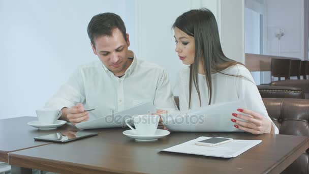 Dos socios de negocios discutiendo el trabajo y sonriendo mientras están sentados en la cafetería — Vídeos de Stock