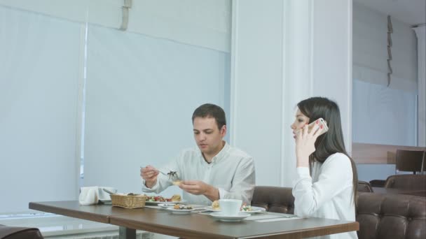 Jovem comendo enquanto sua namorada fala ao telefone no restaurante — Vídeo de Stock