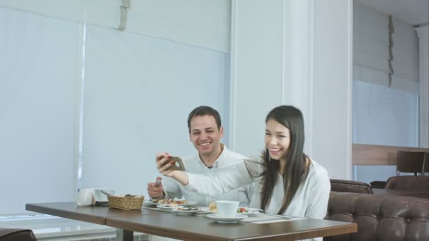 Jovem casal feliz tirando selfies com comida no smartphone em um restaurante — Vídeo de Stock