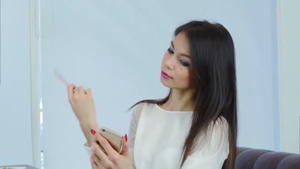 Pretty young girl brushing her hair using phone as a mirror — Stock Video