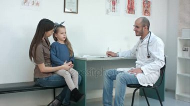 Utangaç küçük kız onun anne kucağa oturma ile konuşurken erkek doktor gülümseyen