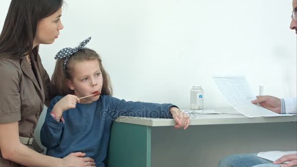 Мужчина-врач объясняет кардиограмму серьезной матери с маленькой девочкой на коленях — стоковое видео