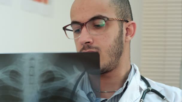 Young male doctor in glasses carefully analyzing xray image — Stock Video