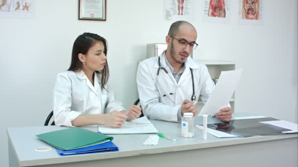 Médico mostrando sua trainee fêmea como ler cardiograma enquanto ela faz anotações — Vídeo de Stock