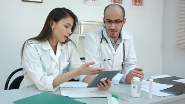 Bastante joven enfermera mostrando algo en la tableta a su colega masculino — Vídeos de Stock