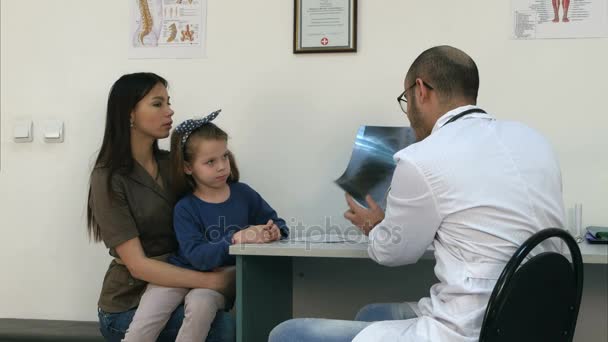 Médico explicando imagen de radiografía de tórax a la madre sosteniendo a su pequeña hija en sus brazos — Vídeos de Stock